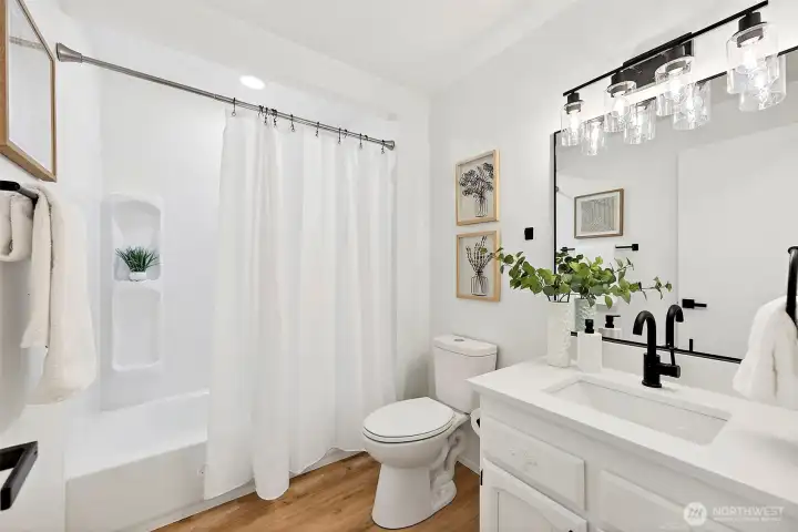 A bright full bath with a tub/shower combo, white quartz vanity, matte black hardware, built-in shower niche, and updated globe lighting throughout.