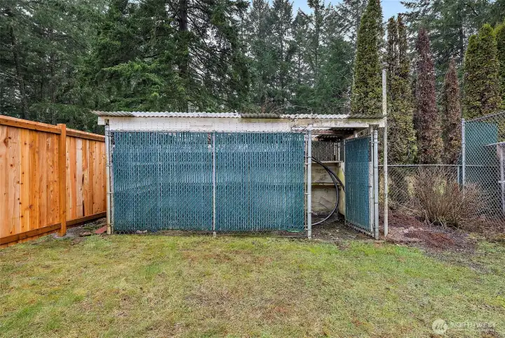 A fenced, covered structure with a corrugated metal roof and concrete base sits along the back fence line, offering flexible use as secure storage, a hobby space, or specialty outdoor enclosure.