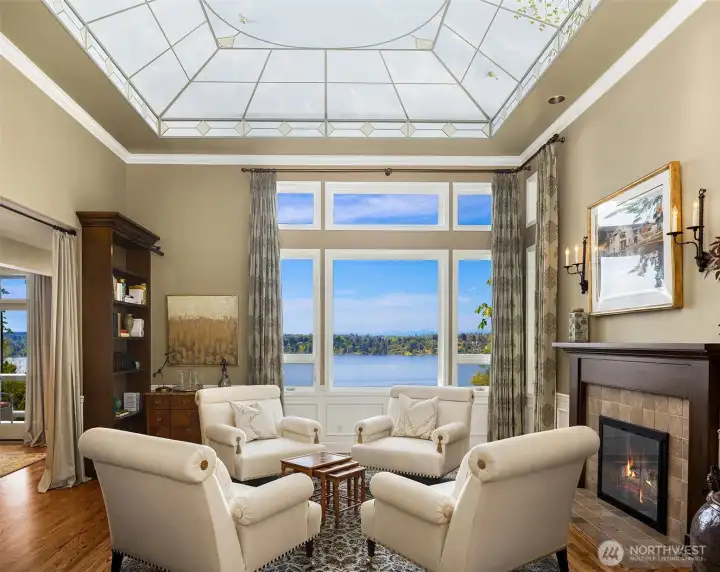 A stunning lakeview sitting room—framed by a dramatic skylit ceiling and anchored by a cozy fireplace, creating the perfect balance of light, warmth, and tranquility.