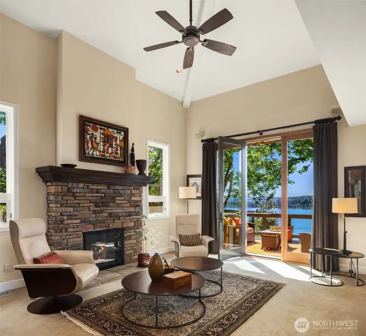Inviting great room with stone fireplace and soaring ceilings, opening to a private outdoor retreat with serene lake and mountain views.