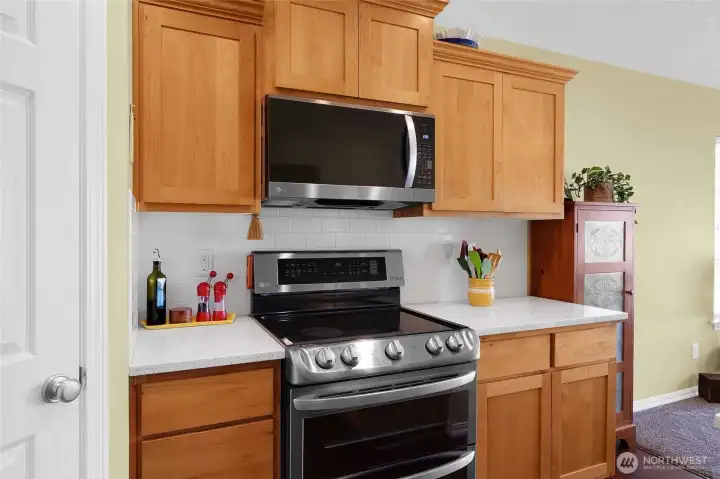 Sleek stainless steel range and microwave pair beautifully with warm wood cabinetry, quartz counters, and crisp tile backsplash, and walk-in pantry.