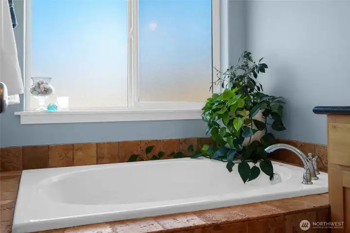 This luxurious tub in the primary bathroom has a Mediterranean style tile color palette. It'll make you feel like you're sitting in luxury with the bubblebath poured in!