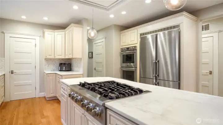 The island anchors the kitchen with a Calacatta marble slab, 6-burner professional gas cooktop, and seating for four. Double wall ovens and the Liebherr column refrigerator are framed by floor-to-ceiling custom cabinetry. Every appliance was selected for a household that cooks seriously.