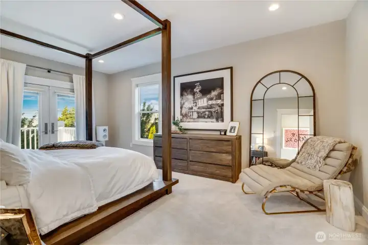 The primary suite opens directly to a private balcony through French doors — treetop views, natural light, and the kind of morning that makes you want to stay in bed longer. A four-poster bed, chaise lounge, and teak dresser furnish a room that reads as a genuine retreat. In-ceiling surround sound is integrated throughout.