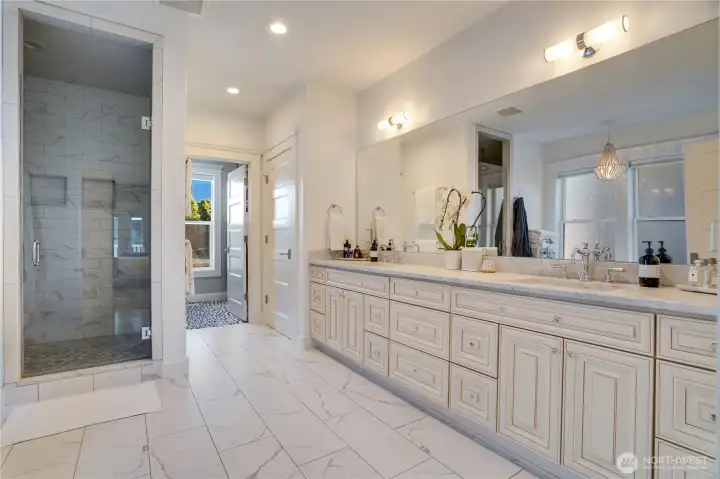 The primary bath at full width — dual vanity with Carrara marble counters and custom glazed cabinetry, Calacatta marble floors, walk-in shower left, and the clawfoot soaking tub suite beyond. This is a bathroom that functions as a destination, not just a utility.