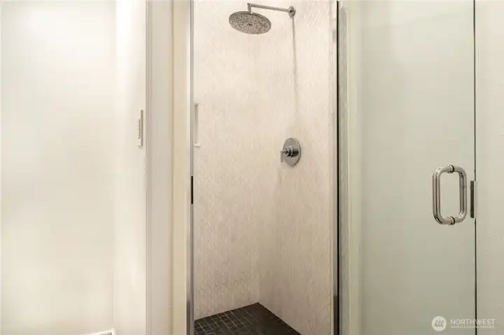 The third floor shower — marble herringbone tile surround floor to ceiling, rain head, frameless glass door with chrome hardware, and dark mosaic tile floor. A dedicated bath on the third floor means the media room, flex office, and two bedrooms function as a fully self-contained suite. No sharing with the floors below.