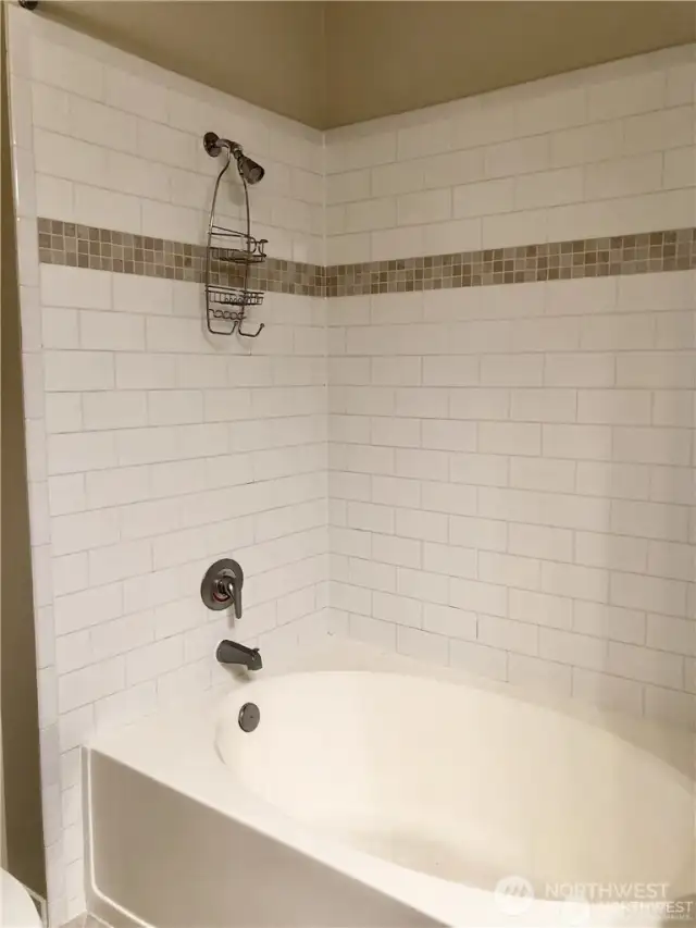 Artistic tile surround on extra-large soaking tub in primary bathroom.