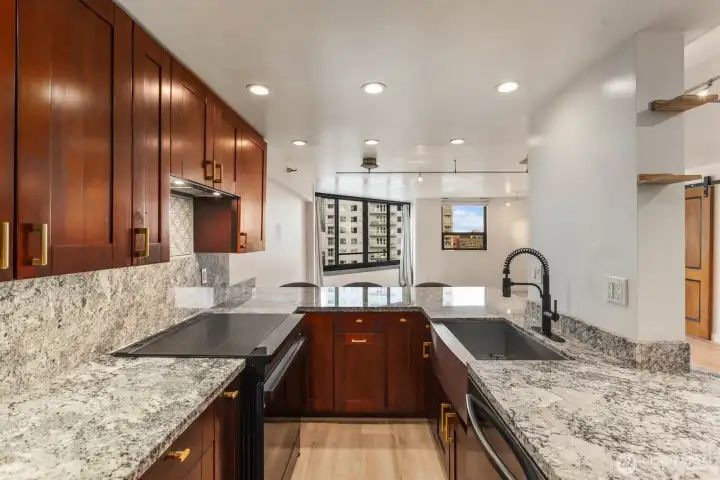 Chef-style kitchen featuring wraparound stone countertops, sleek cooktop, generous prep space, and a seamless flow into the dining and living area.