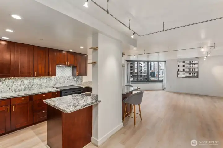 Open concept Seattle condo kitchen and living space featuring a large kitchen peninsula, warm wood cabinetry, and expansive windows bringing natural light into the main living area.