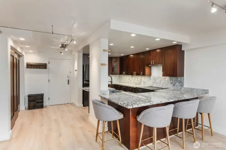 Open concept kitchen with granite peninsula seating, wood cabinetry, recessed lighting, and direct connection to the entry and main living space.