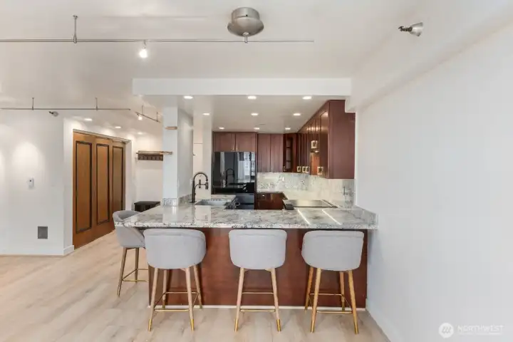 Seattle condo kitchen with large granite breakfast bar, apron front sink, wood cabinetry, and seating that opens directly into the main living area.