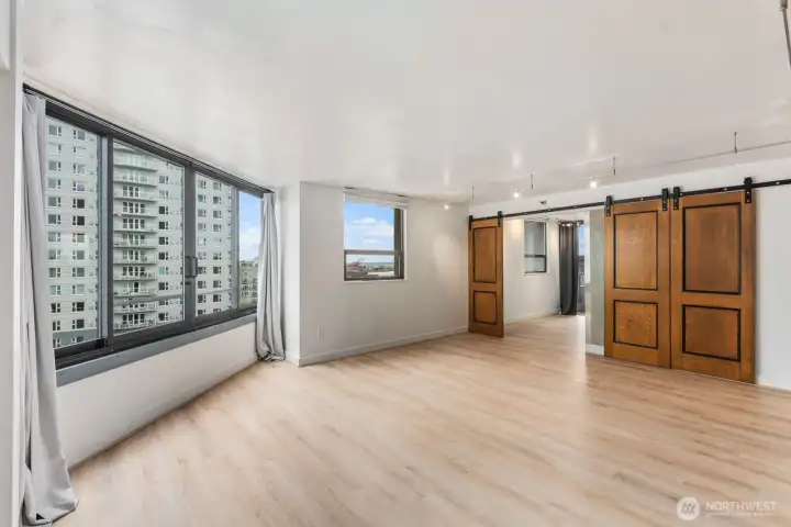 Seattle condo living area with oversized windows capturing nearby city skyline views and sliding wood barn doors separating the adjacent room.