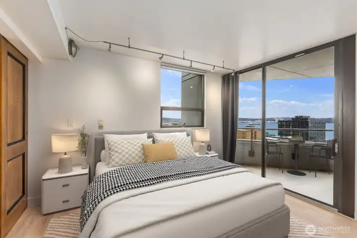 Virtually staged Seattle condo bedroom with sliding glass doors leading to a private balcony and Puget Sound water views visible beyond nearby buildings.