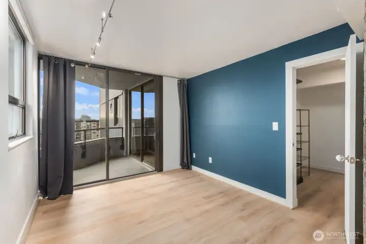 Seattle condo bedroom with sliding glass doors leading to a private balcony, large windows bringing in natural light, and walk-in closet access.
