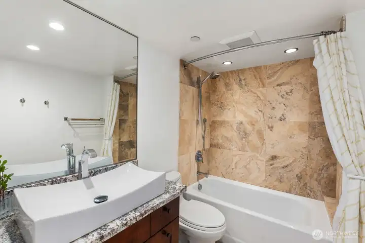 Seattle condo bathroom with single sink vanity, large mirror, and tub shower featuring full wall tile surround.