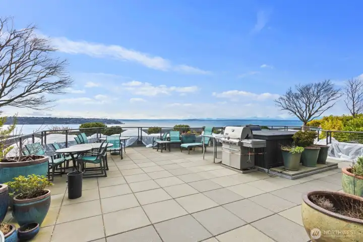 Shared rooftop deck with outdoor dining tables, seating areas, and sweeping Puget Sound water views across the horizon
