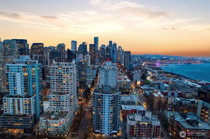 Downtown Seattle aerial skyline view looking toward Elliott Bay with waterfront attractions, illuminated city buildings, and the Seattle Great Wheel along the pier.