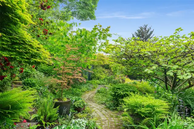 A winding brick path leads through the tranquil, well established gardens