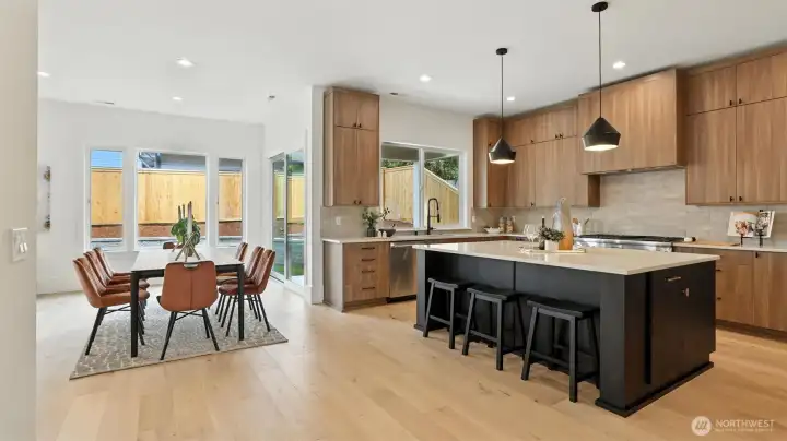 Designed for the way people truly live — connected, open, and beautifully balanced. The kitchen showcases full-height cabinetry, quartz counters, and a striking black island with informal seating. Pendant lighting adds architectural polish, while expansive windows flood the space with natural light. Adjacent, the dining area feels warm and modern, anchored by warm floors and a wall of glass that opens to the backyard — creating seamless indoor-outdoor flow for entertaining and everyday living.