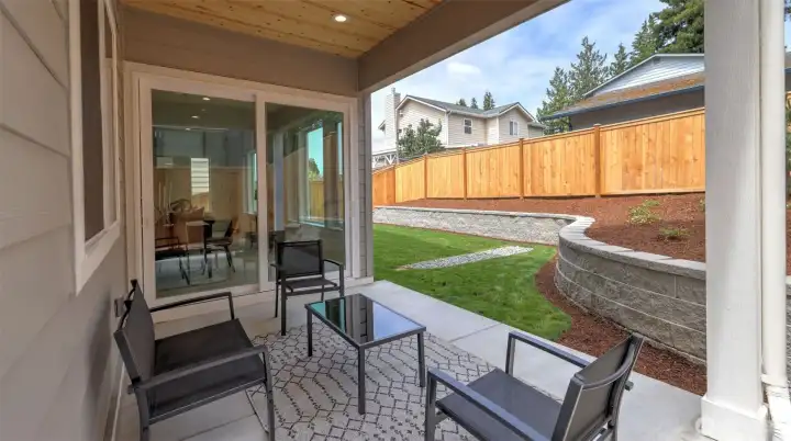 Expansive sliding doors open to a covered patio that extends living space outdoors — perfect for morning coffee or evening gatherings. The landscaped, fully fenced backyard is defined by tiered stonework and clean architectural lines, offering both beauty and privacy. With a lush lawn, sprinkler system and covered seating area, it’s a natural extension of the home’s bright, welcoming interior.