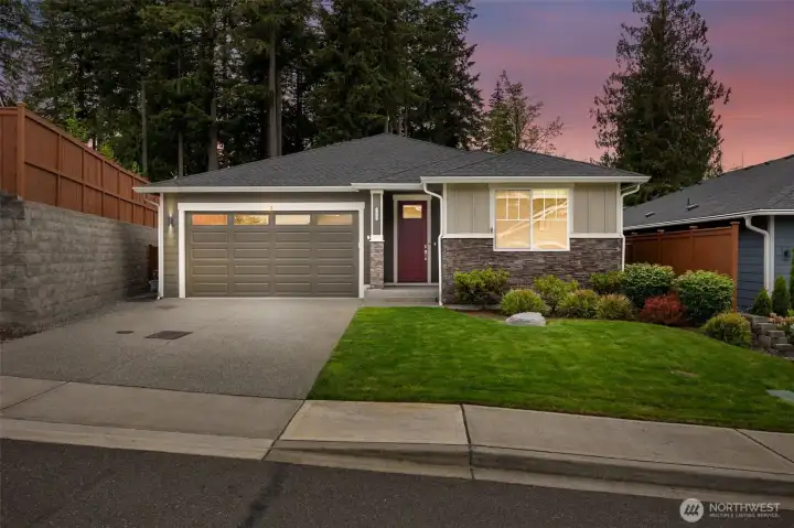 There is something about a twilight photo that tells you whether a house feels like a home, and this one passes the test beautifully. The covered front entry glows warmly beneath the evening sky, creating a welcoming first impression for both guests and homeowners alike. The architectural lines of the composition roof add visual interest and complement the home's blend of stone and durable siding, while the covered porch offers a practical place to greet visitors, collect deliveries or simply stay dry during one of those classic Pacific Northwest drizzles.