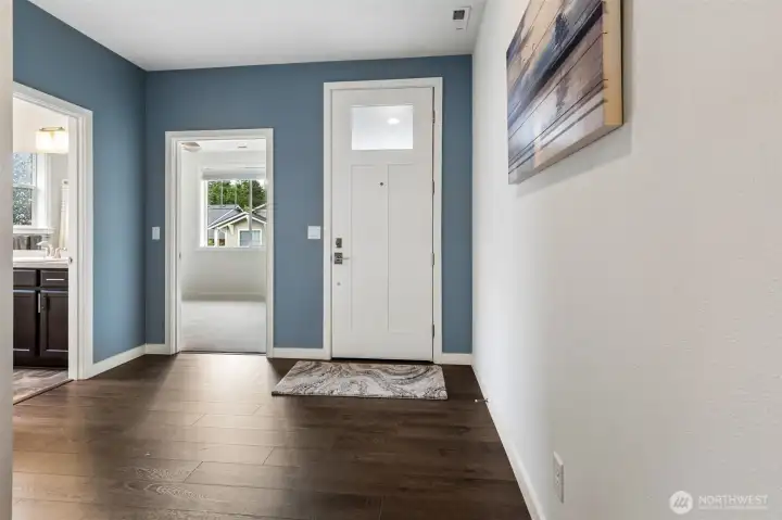 The foyer offers a warm and welcoming first impression with beautiful wide-plank laminate flooring in a rich dark walnut tone that brings instant warmth and character to the space. The handsome front door features a privacy glass insert that allows natural light to filter inside while still maintaining a comfortable sense of seclusion from the street. You can also see the thoughtful layout of the front guest wing, with the front bedroom located just off the entry and the nearby bathroom positioned conveniently beside it. Whether hosting overnight guests, family visits or creating a dedicated office space, this arrangement allows visitors to come and go comfortably without needing to pass through the more private areas of the home.
