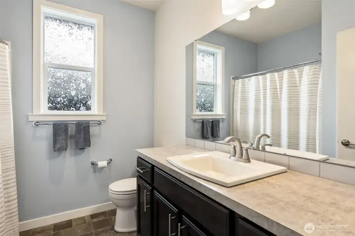 This full bathroom is perfectly positioned between the two front bedrooms, creating an ideal guest wing tucked right off the foyer. One of the most desirable features of this floorplan is its split-bedroom design, which places the primary suite on the opposite side of the home for an extra level of privacy when hosting overnight guests or visiting family. Soft whisper-blue walls create a calm, spa-like atmosphere, while the double-hung window features privacy glass that allows natural light to brighten the space without sacrificing comfort. Convenient, cheerful and thoughtfully located, this bathroom helps the front portion of the home function almost like its own private guest retreat.