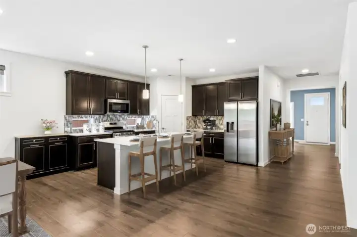 This wider view of the kitchen gives a great sense of how effortlessly the floorplan flows from one space to the next. The foyer and hallway connect naturally to the heart of the home, creating a layout that feels open and inviting without sacrificing definition between spaces. One of the thoughtful upgrades you'll appreciate every day is the addition of dimmer switches in both the kitchen and living room areas, allowing you to customize the lighting whether you're hosting friends, preparing dinner or settling in for a quiet evening at home.