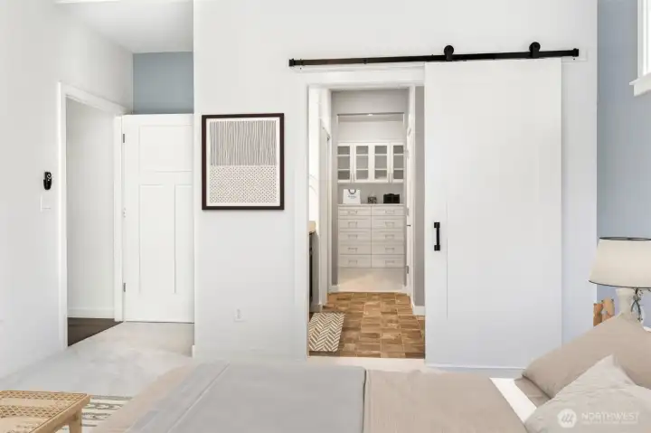 This view into the primary bath highlights one of the smartest features of the suite's design: the ability for two people to comfortably share the space without getting in each other's way. With the walk-in closet located beyond the barn door, someone can get completely dressed and ready for the day while their partner continues sleeping peacefully in the bedroom. The spacious glass-enclosed shower features a low-threshold walk-in entry for easier access and a clean, modern look, while the overall layout feels both functional and thoughtfully planned.