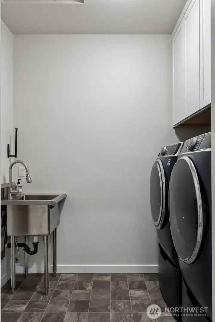 This laundry room proves that even practical spaces deserve a little style. Located just off the mudroom entry, it's perfectly positioned to handle everything from beach towels to gardening clothes without hauling them through the house. A handsome stainless-steel utility sink with pull-down faucet makes cleanup a breeze, while the installed paper towel holder is already ready for action because somebody here clearly appreciated efficiency. The high-efficiency GE Profile washer and dryer stay with the home and are elevated on pedestals, making loading and unloading noticeably easier on your back. Newer cabinetry adds both storage and visual appeal, creating a laundry room that feels thoughtfully upgraded rather than simply functional.