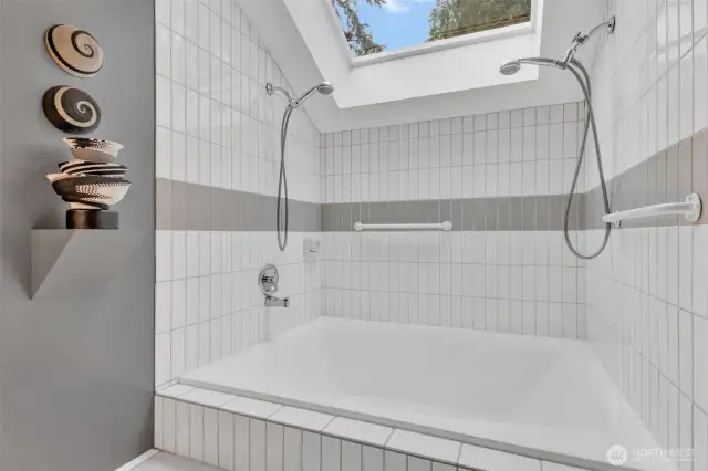 Primary bath is anchored by oversized soaking tub with dual shower heads, all drenched in light from large overhead skylight