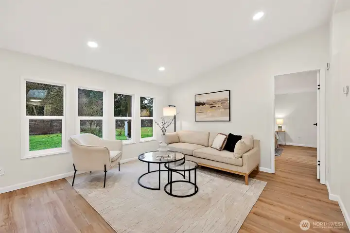 A comfortable, light-filled living area with dual windows overlooking the yard, LVP flooring, and recessed lighting throughout.