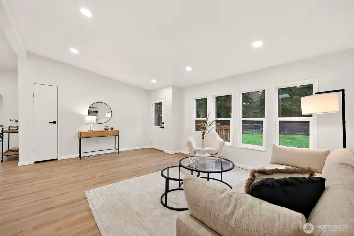 Generous living room with triple windows, recessed lighting, LVP flooring, and open sightlines to the entry and adjoining spaces.