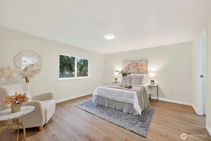 A peaceful primary suite with LVP flooring, a large window with yard views, recessed lighting, and a generous layout with sitting area.