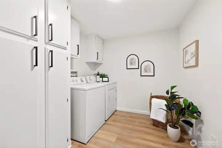 Dedicated laundry room with full-size washer and dryer, white cabinetry with black hardware, and LVP flooring — functional and well-appointed.