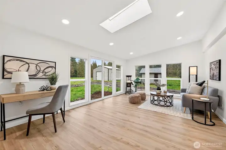 Expansive bonus room flooded with natural light from a skylight, sliding glass door, and large picture windows overlooking the yard and outbuildings.
