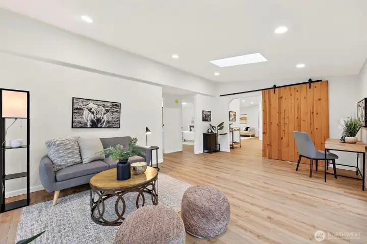 Generous bonus living room with a skylight, recessed lighting, LVP flooring, and a statement sliding barn door — open to bedrooms and the main living area.