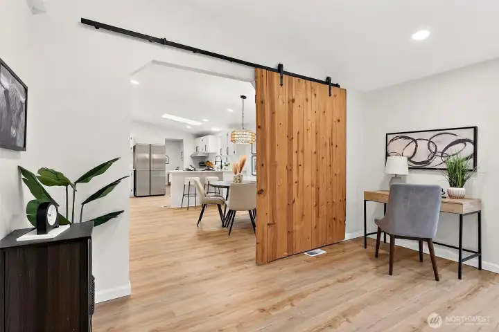 A striking wood sliding barn door on black hardware separates the bonus room from the main living area, with open views to the kitchen and dining beyond.
