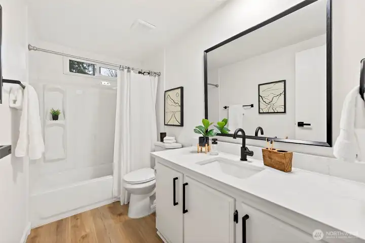 Updated full bath with white shaker vanity, quartz countertop, black hardware, large framed mirror, and a tub/shower combo with a built-in niche.
