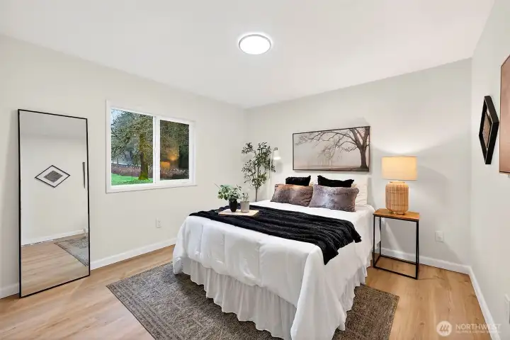 Well-sized bedroom with LVP flooring, a bright window with yard views, and a neutral palette — ideal as a guest room or secondary bedroom.