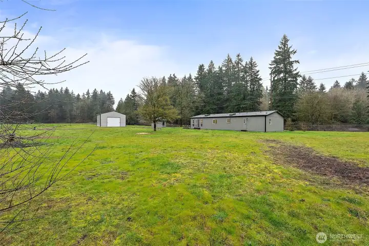 Wide view of the property showcasing the home, detached garage, and open green acreage surrounded by mature evergreens — a peaceful, private setting.