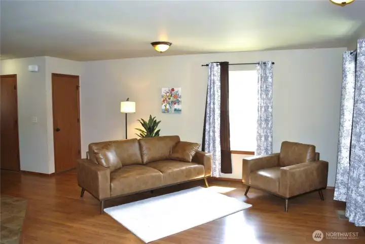Inviting living room filled with natural light and designed for comfortable everyday living. The open-concept layout creates a seamless flow between the living area and kitchen, while large windows enhance the bright and airy feel. Durable laminate flooring, neutral finishes, and an efficient use of space make this room both functional and welcoming. A perfect place to relax, entertain, or enjoy quiet evenings at home.