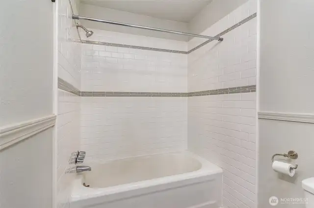 Another view of the bathroom, highlighting the tub and clean white tiling.