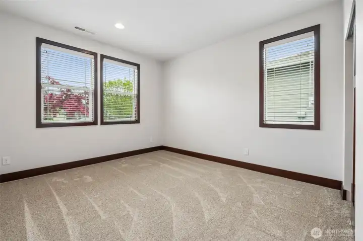 2nd bedroom with new carpet, located in the front of the home, opposite end of the primary room, looking out at the gorgeous multi-colored flowers just outside.