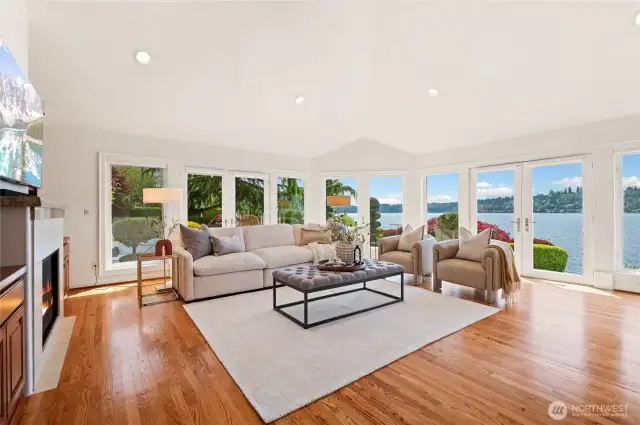 Formal living room with cathedral ceilings, wrap-around wall of windows, cozy fireplace, and built-ins.