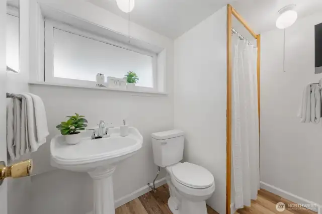 The lower-level bathroom includes a pedestal sink, walk-in shower, and frosted window for added privacy and natural light. Durable vinyl flooring and simple finishes make this space both functional and easy to maintain.