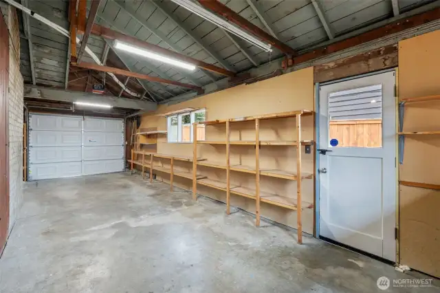 The attached garage features built-in shelving for organized storage and ample space for parking or a workshop setup. Exposed beams and overhead lighting provide a functional and accessible workspace.