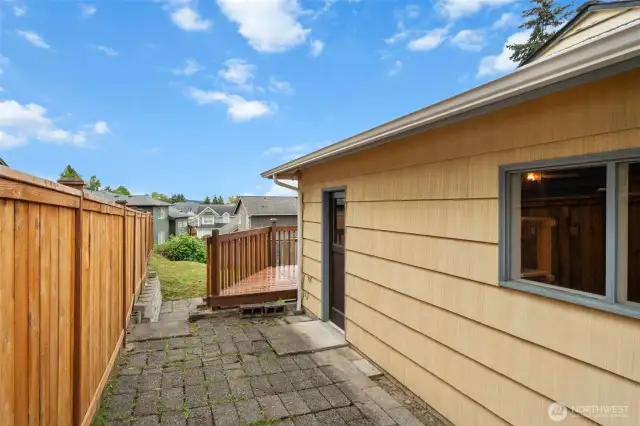 This exterior door provides direct access to the garage, offering convenience for storage or workshop use. The adjacent walkway and steps lead up to the backyard deck and lawn area.