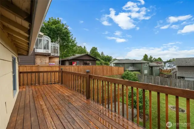 The elevated deck overlooks a fenced backyard with a fire pit area, offering a great space for outdoor gatherings. Wood railings and open views provide both safety and a sense of connection to the community!