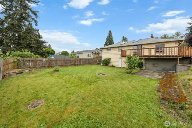 Looking across the backyard, you’ll find a spacious green lawn framed by wood fencing and a few established planting beds. The layout provides flexibility for outdoor activities or future landscaping ideas.